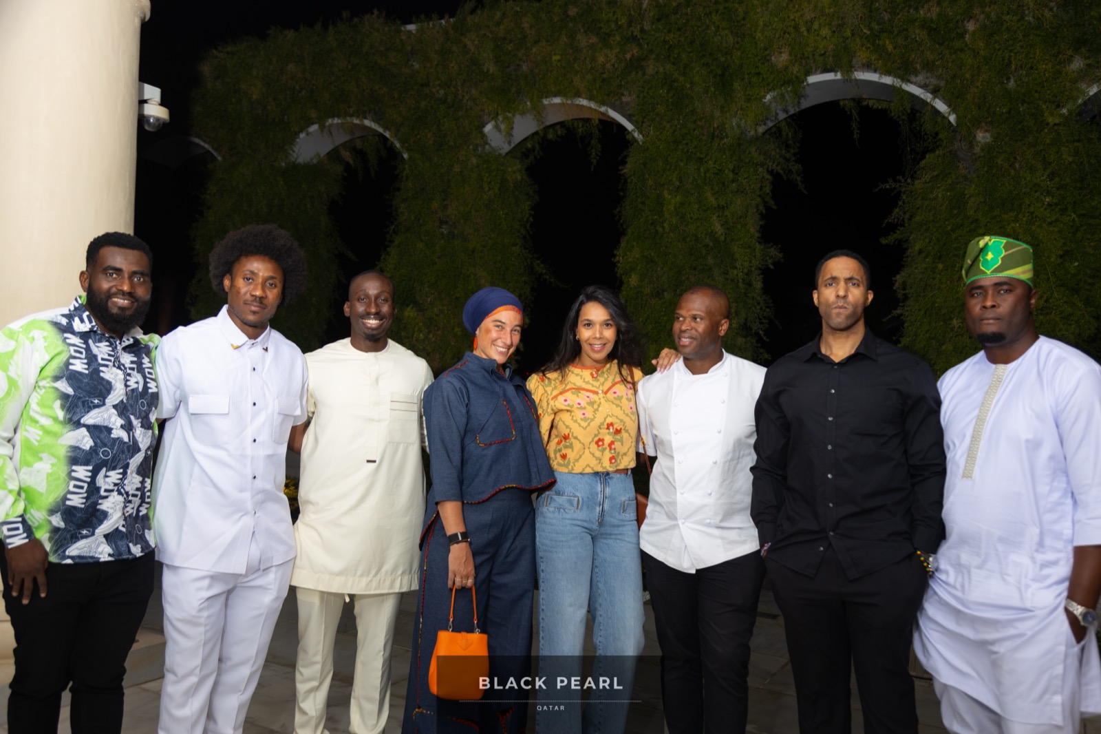 A diverse group of eight Black Pearl guests in African formal and contemporary dress together at an evening gathering