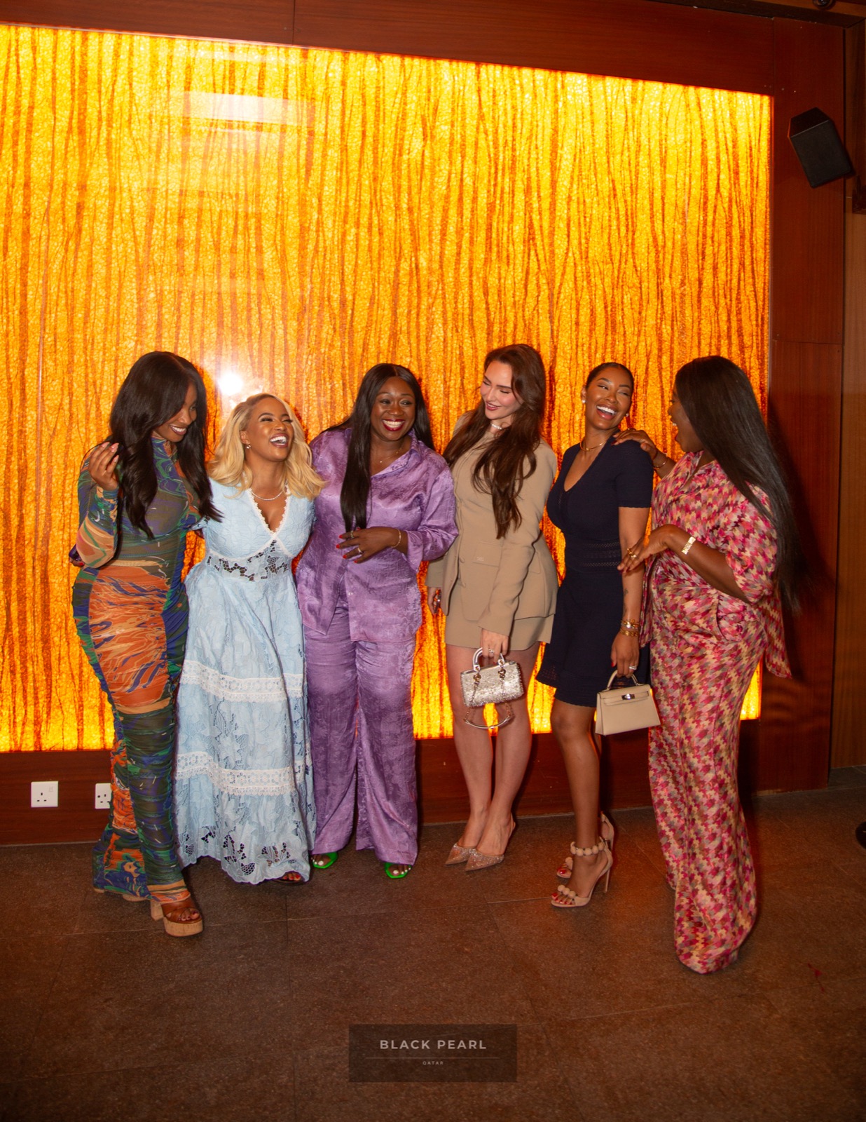 Six Black Pearl guests laughing together against a warmly lit amber wall