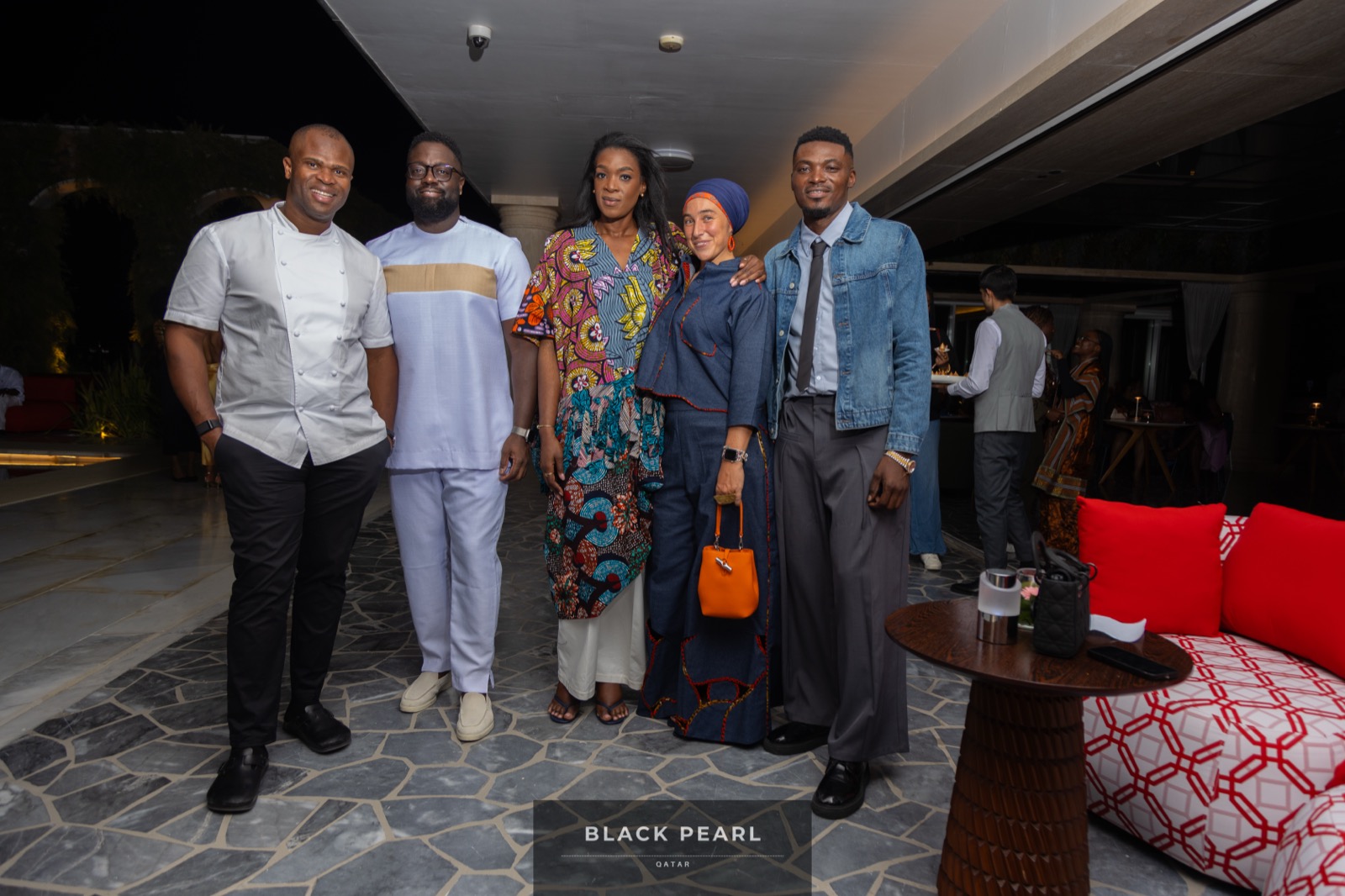 A group of five Black Pearl guests in vibrant African formal dress smiling together